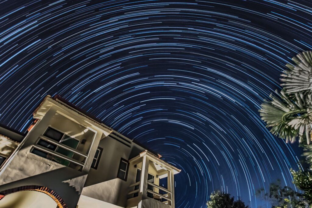 star trails in the night sky over a white stucco villa.
