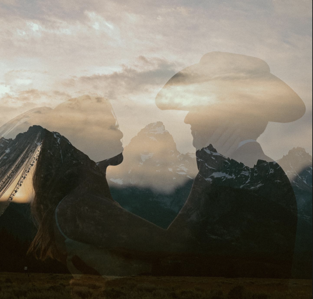 A double-exposure photo, with a mountain range overlaid on an image of a couple in wedding attire embracing each other.